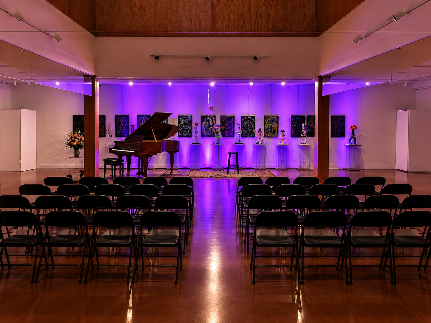 The Museum's first-floor gallery set up for an event, with a piano, rows of chairs, and sculpture displays lit in purple